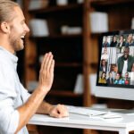 Man waving during a video call on desktop computer in a home office setting