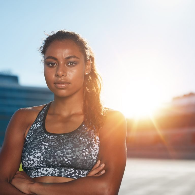 Confident female athlete standing outdoors in the sun with arms crossed